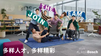 两名员工坐在一张桌子边用各自的显示器协作编程，并相互碰杯。