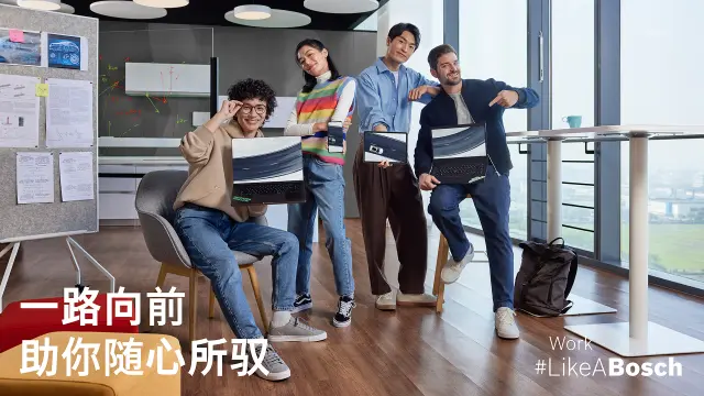 一名员工在展示架前摆姿势拍照，展示架上摆满了印有博世相关图案的帽子，例如“Work #LikeABosch”主题。